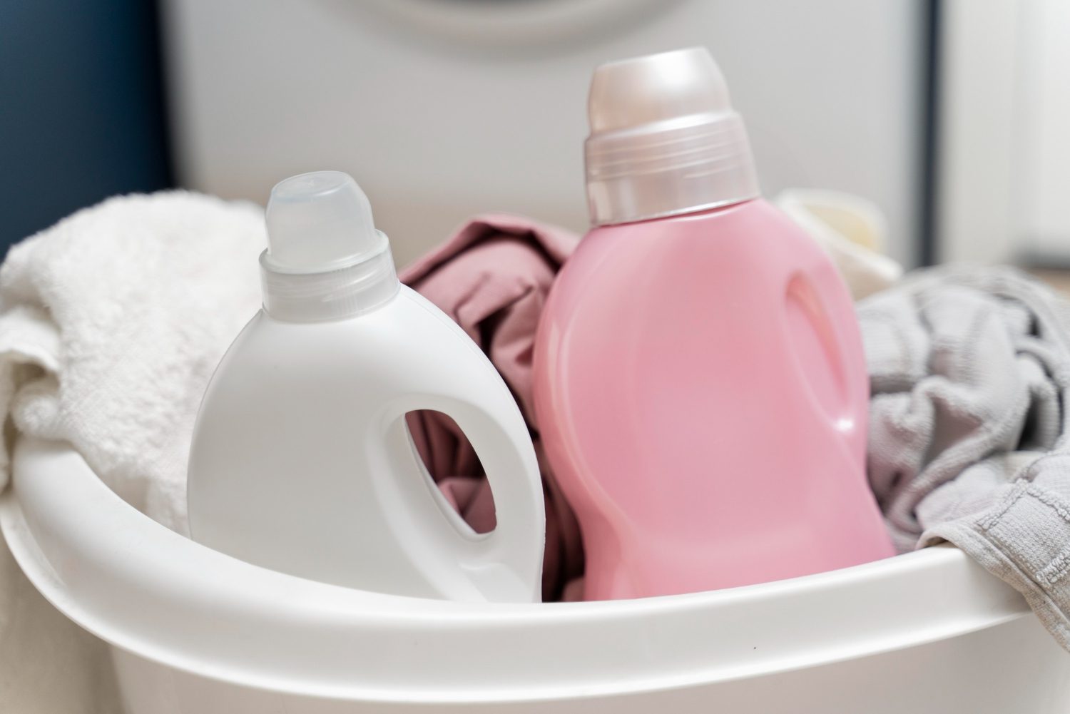 A woman in glasses examines clothes from a laundry basket in front of industrial washing machines at a laundromat.