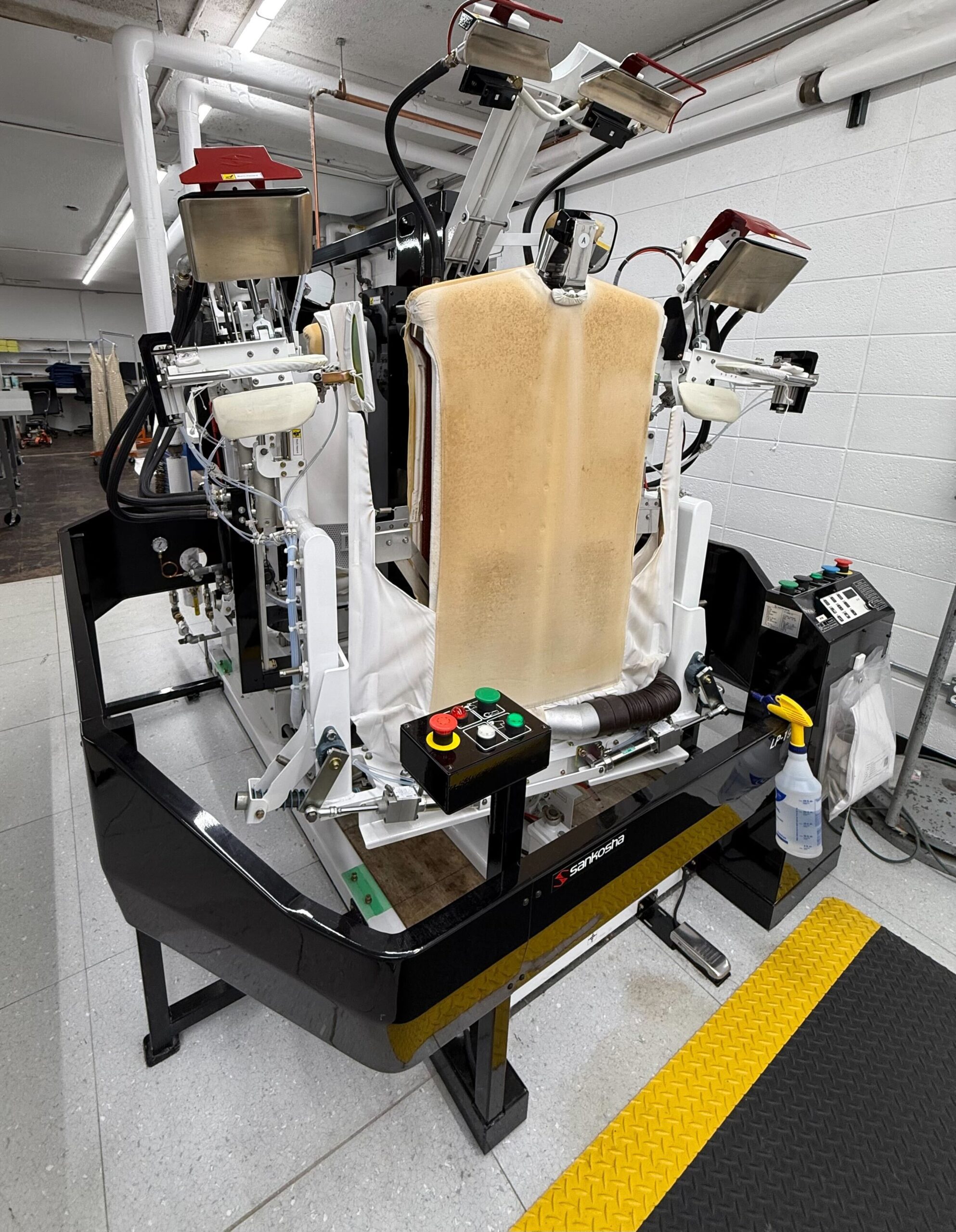 A commercial pressing machine with padded boards, control buttons, and spray bottle in an industrial laundry setting.